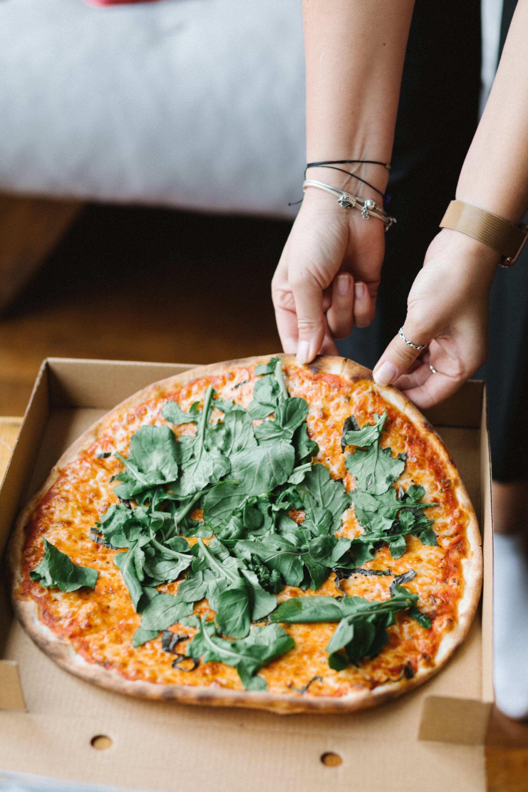 Vue en plongée d'une pizza et deux mains qui tente de prendre une partie de la pizza.