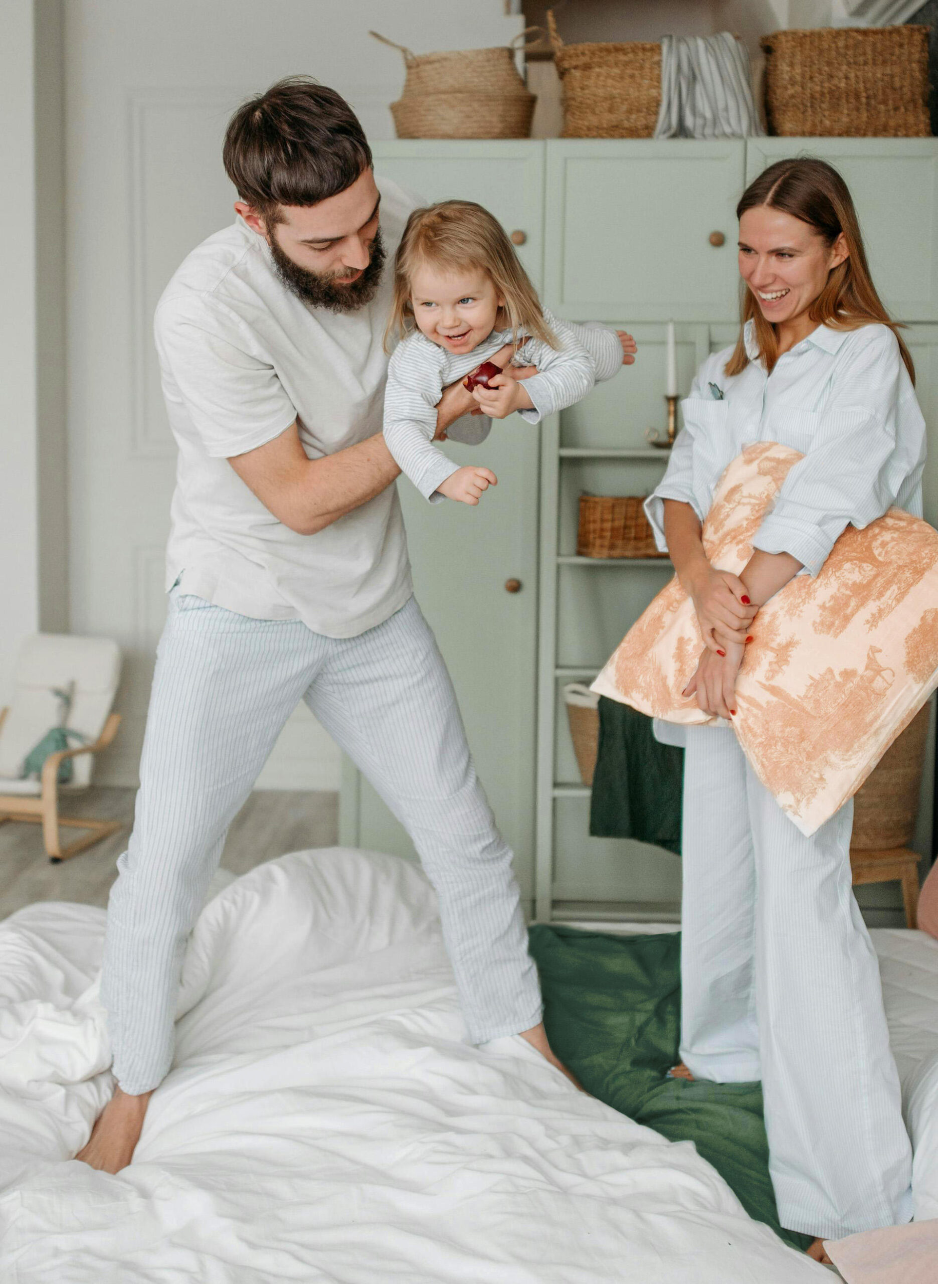 Famille (papa, maman et petite fille) tous habillés de blanc. Le papa joue avec la petite fille dans ses bras.